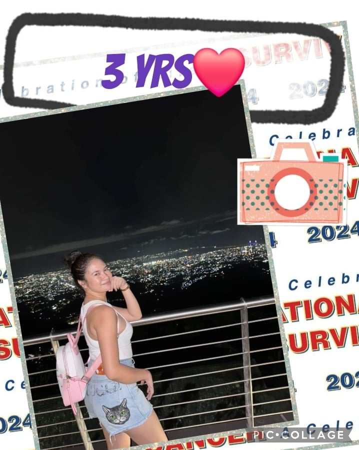 Young woman in a light tank top and denim shorts stands smiling at a nighttime city view, celebrating three years of survival.