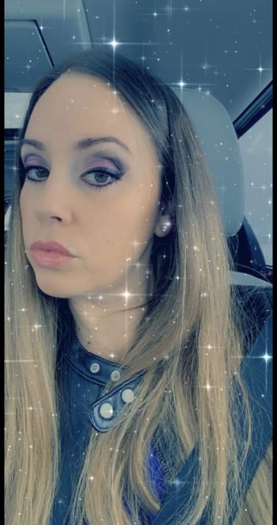 A woman with long, straight hair and subtle makeup poses in a car, sparkling effects overlaying the image to enhance its vibrancy.