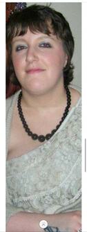 Woman with short brown hair and subtle makeup, wearing a light-colored dress and a beaded necklace, poses confidently for the camera.