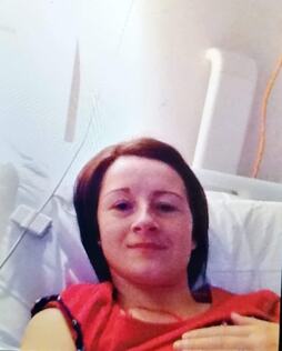 Young woman smiling while lying in a hospital bed, wearing a red shirt, suggesting recovery or a visit. Relevant to health and wellness topics.