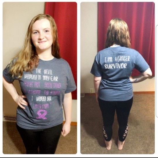 A smiling young woman poses in a gray t-shirt, front and back showing the text "The devil whispered in my ear..." and "I am a cancer survivor," symbolizing strength and resilience.